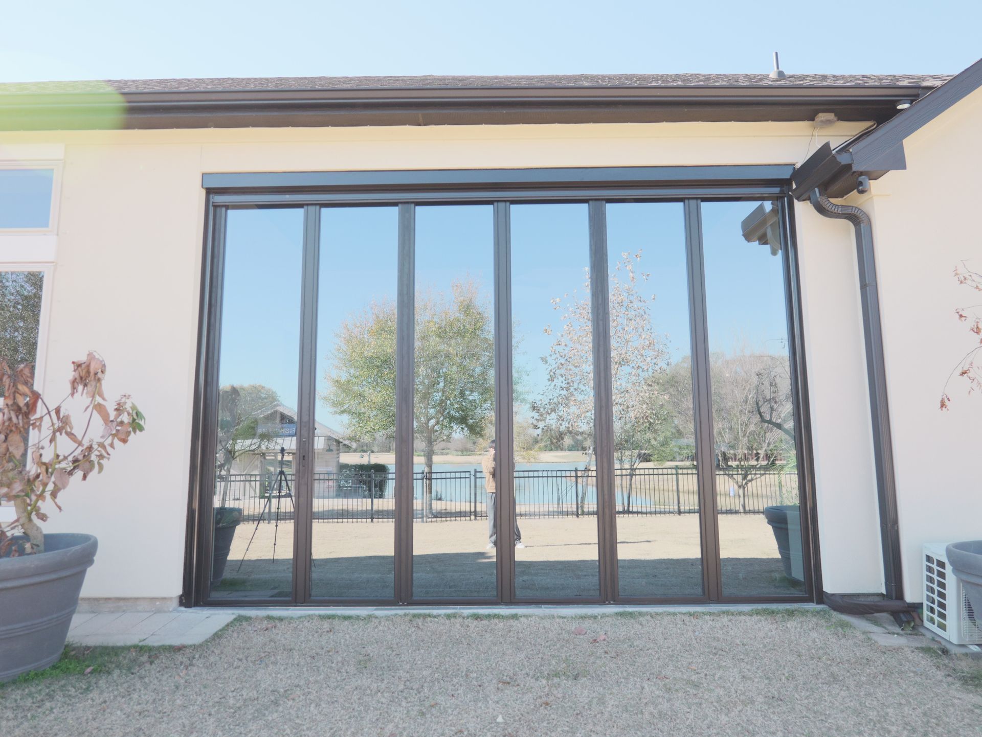 Large black-framed glass sliding doors on a white house exterior, reflecting trees and a fenced yard.