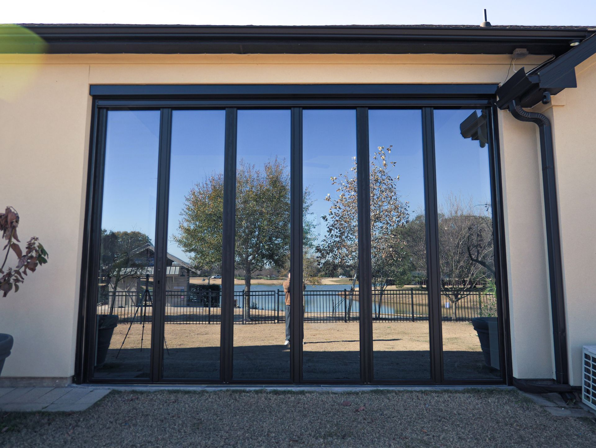 Large black-framed glass doors on a beige wall, opening to a sunny outdoor patio and trees beyond.