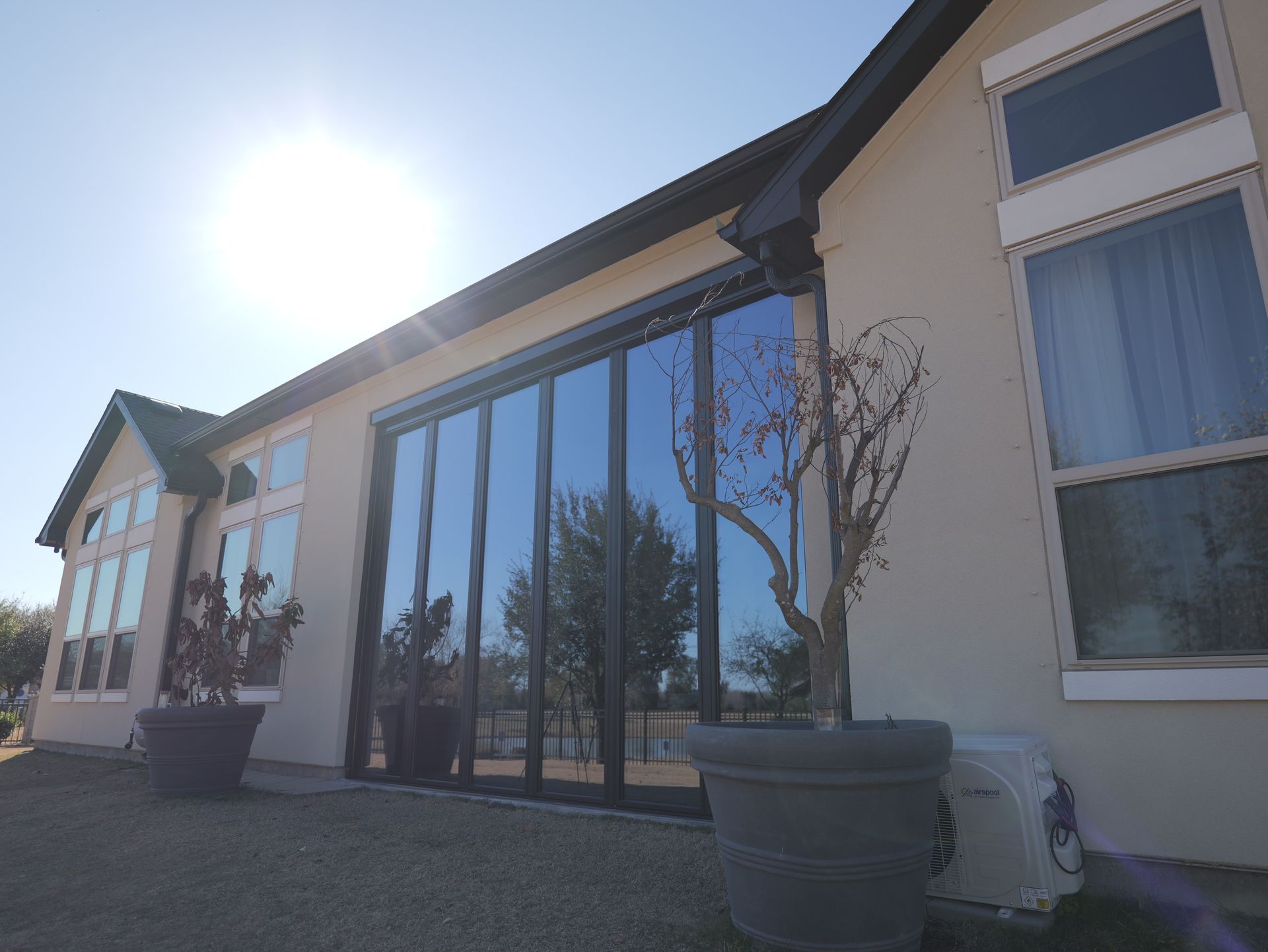 Modern house exterior with large glass doors, potted plants, and bright sunlight.