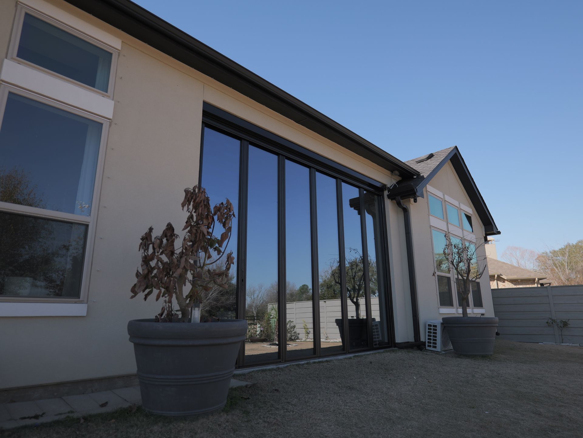 Modern house exterior with glass sliding doors, large potted plants, and a gravel yard.