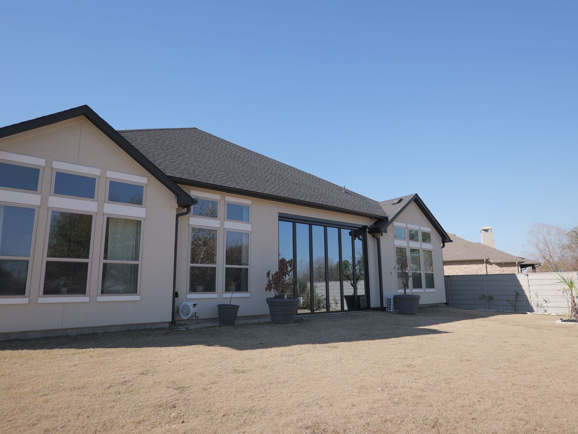 Single-story house with large windows and a gravel yard under a clear blue sky
