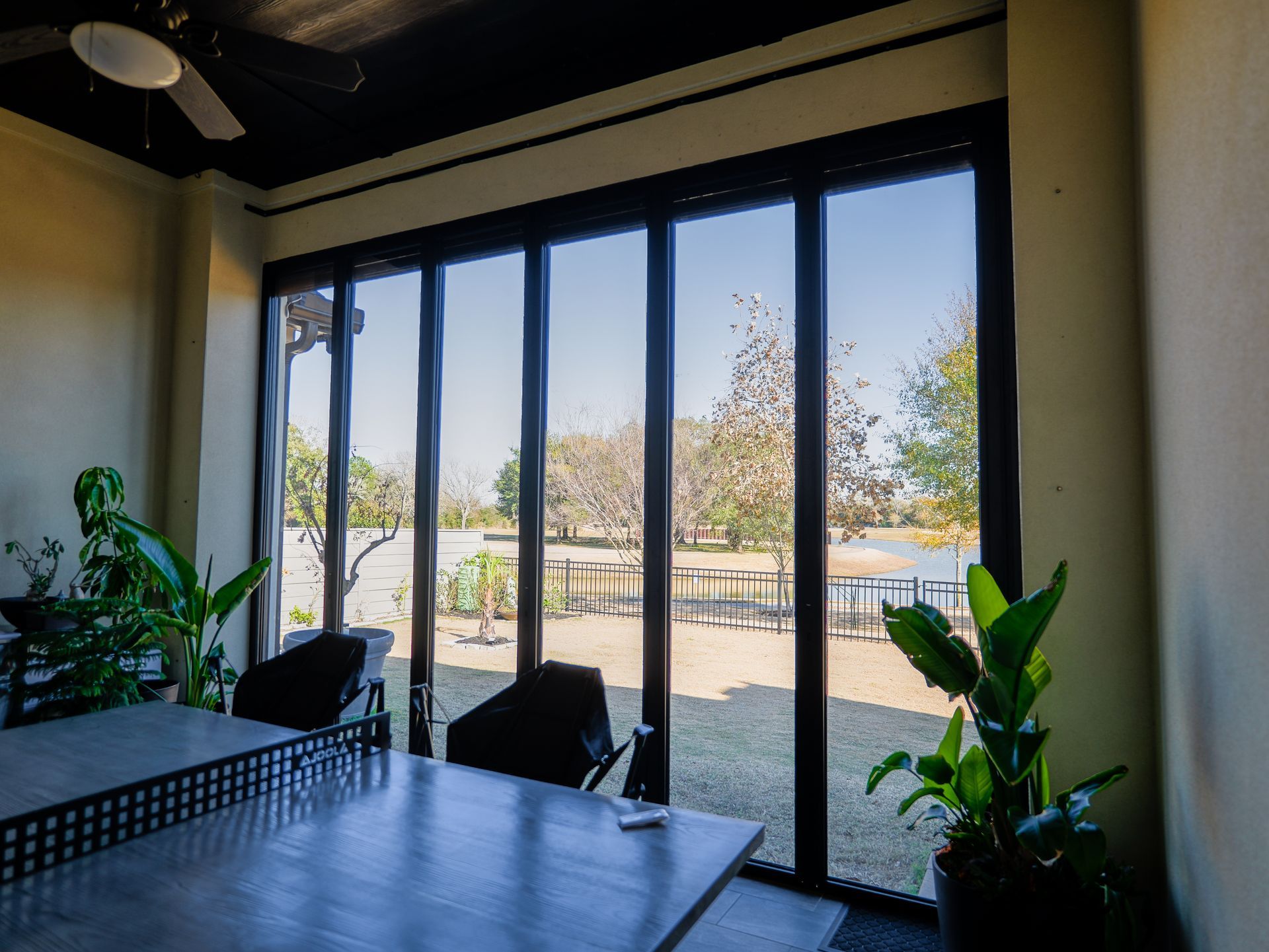 Modern room with glass doors opening to a sunny patio and outdoor seating, with plants by the window.