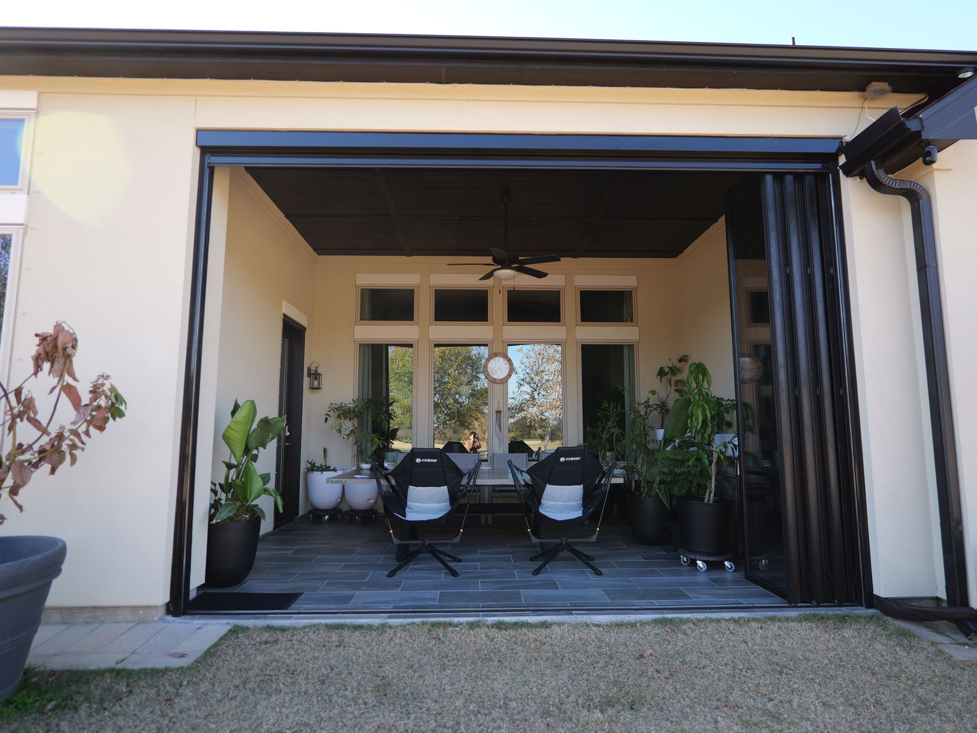 Covered patio with outdoor seating, potted plants, and open sliding doors to a home interior.