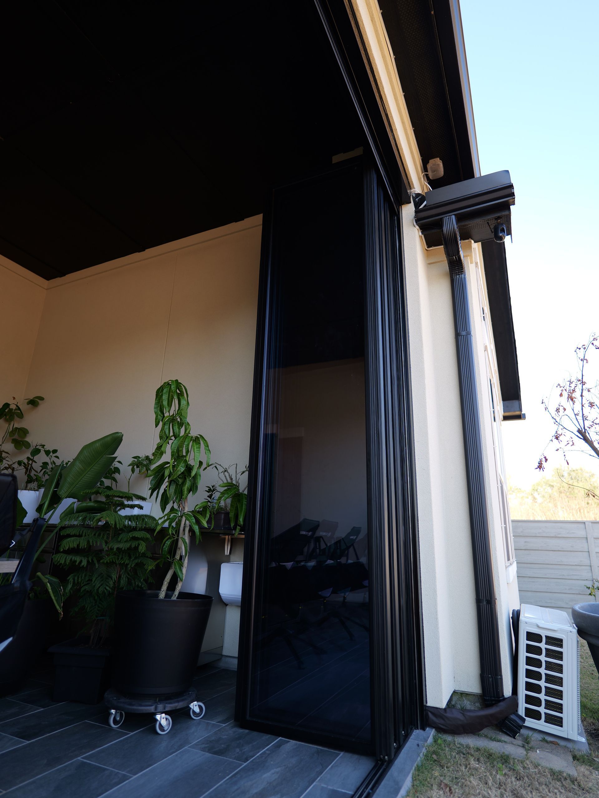 Outdoor patio with potted plants beside a dark sliding glass door and white air conditioner unit