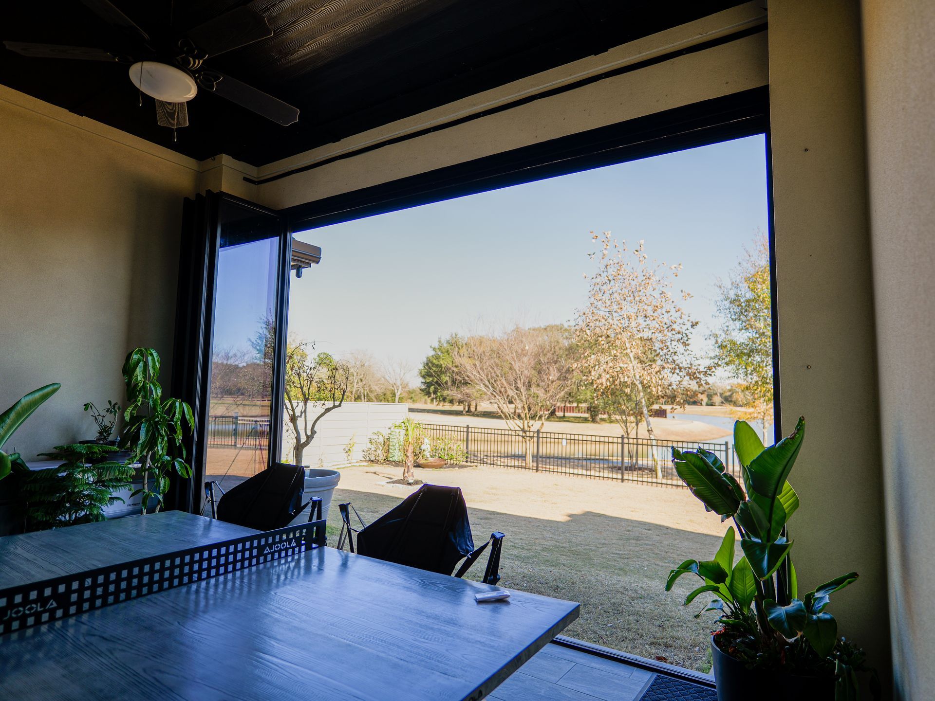 Covered patio overlooking a sunny yard with a pool, outdoor table, and potted plants