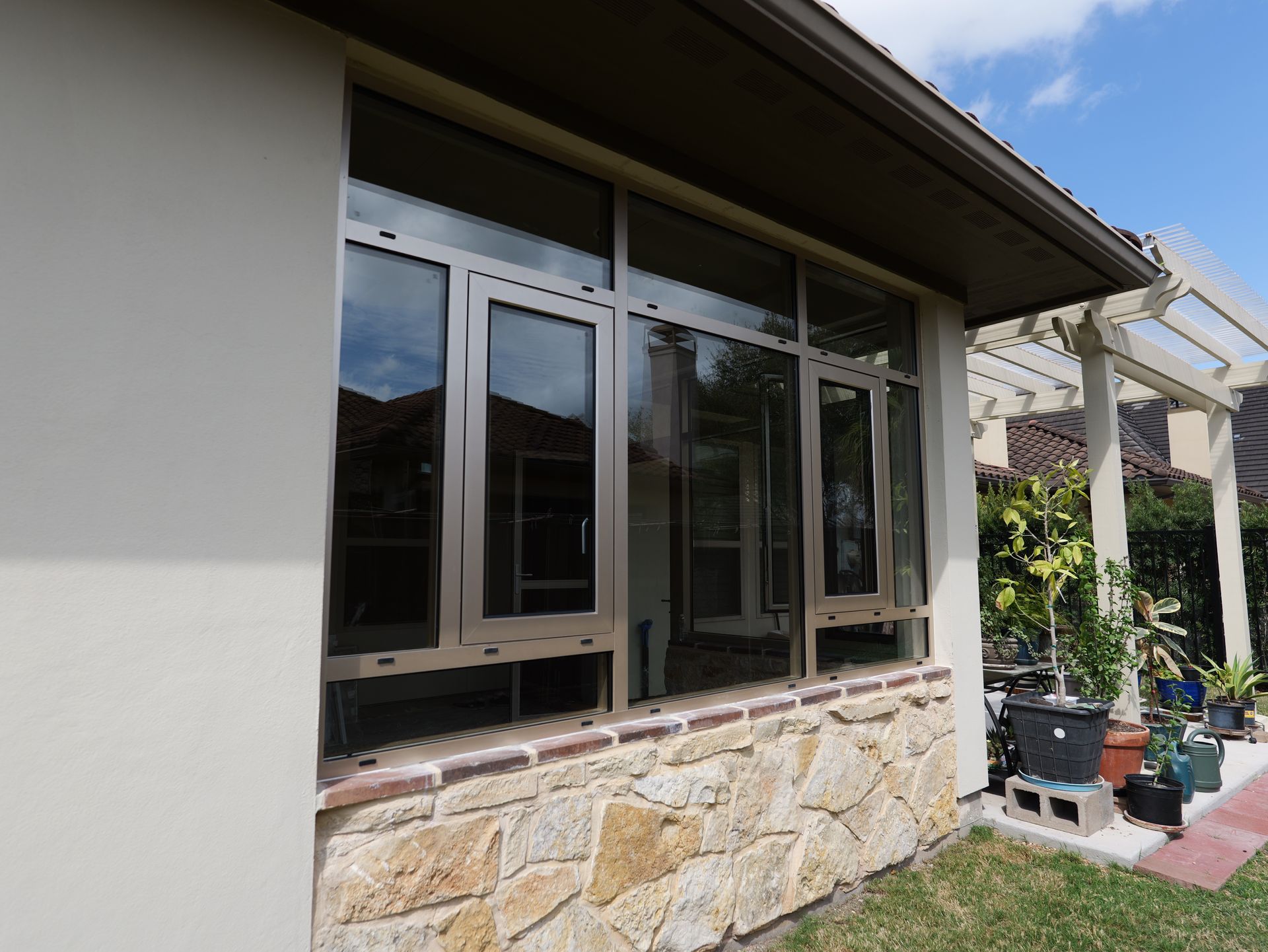 House exterior with large windows, stone lower wall, and a covered patio area