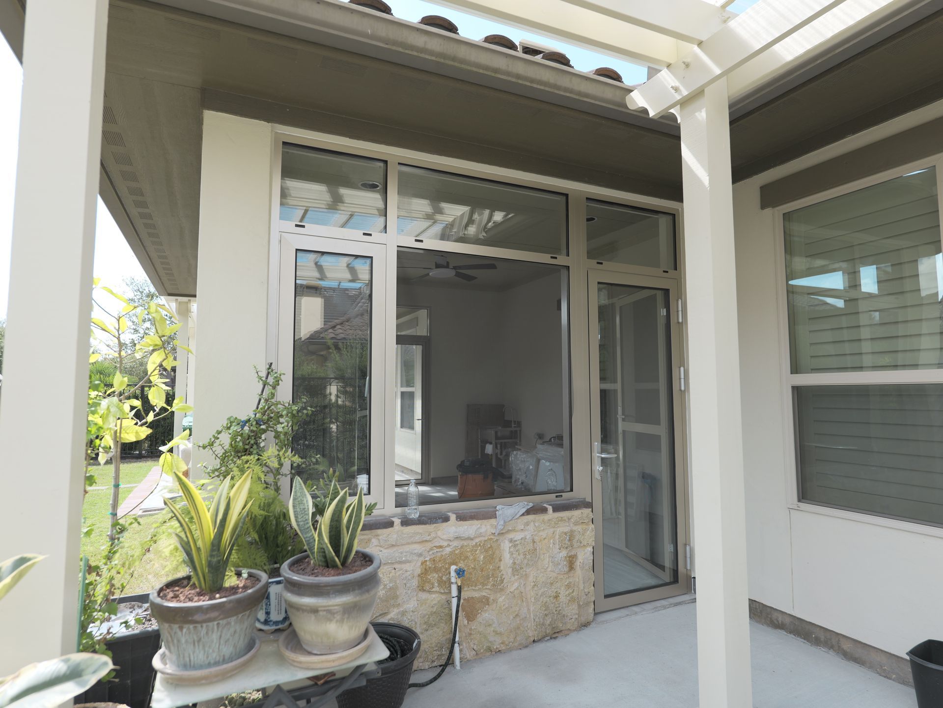 Covered patio with potted plants, sliding glass doors, and a stone half-wall seating area.