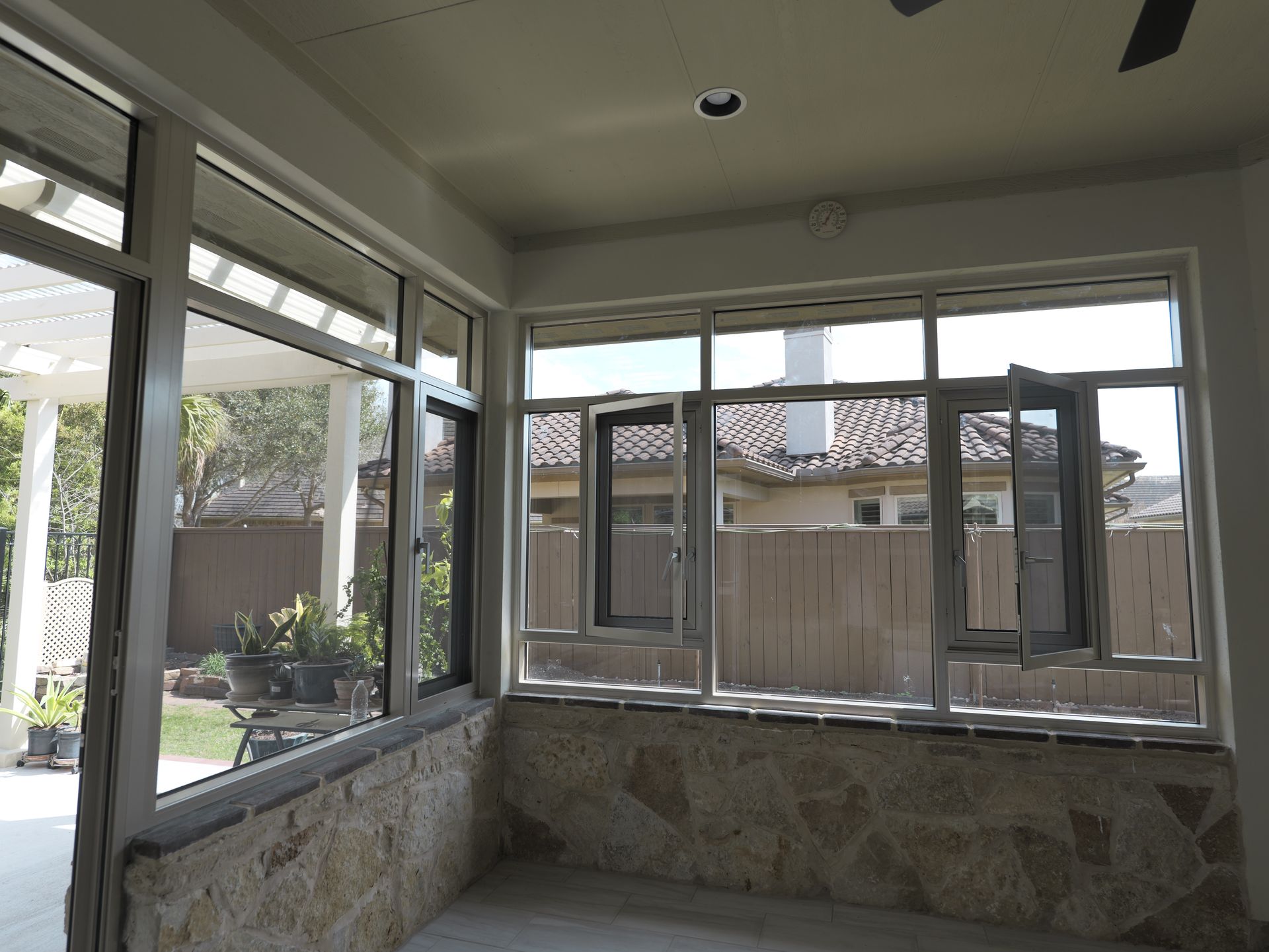 Sunroom with large windows, stone half-walls, and a view of a fenced backyard.