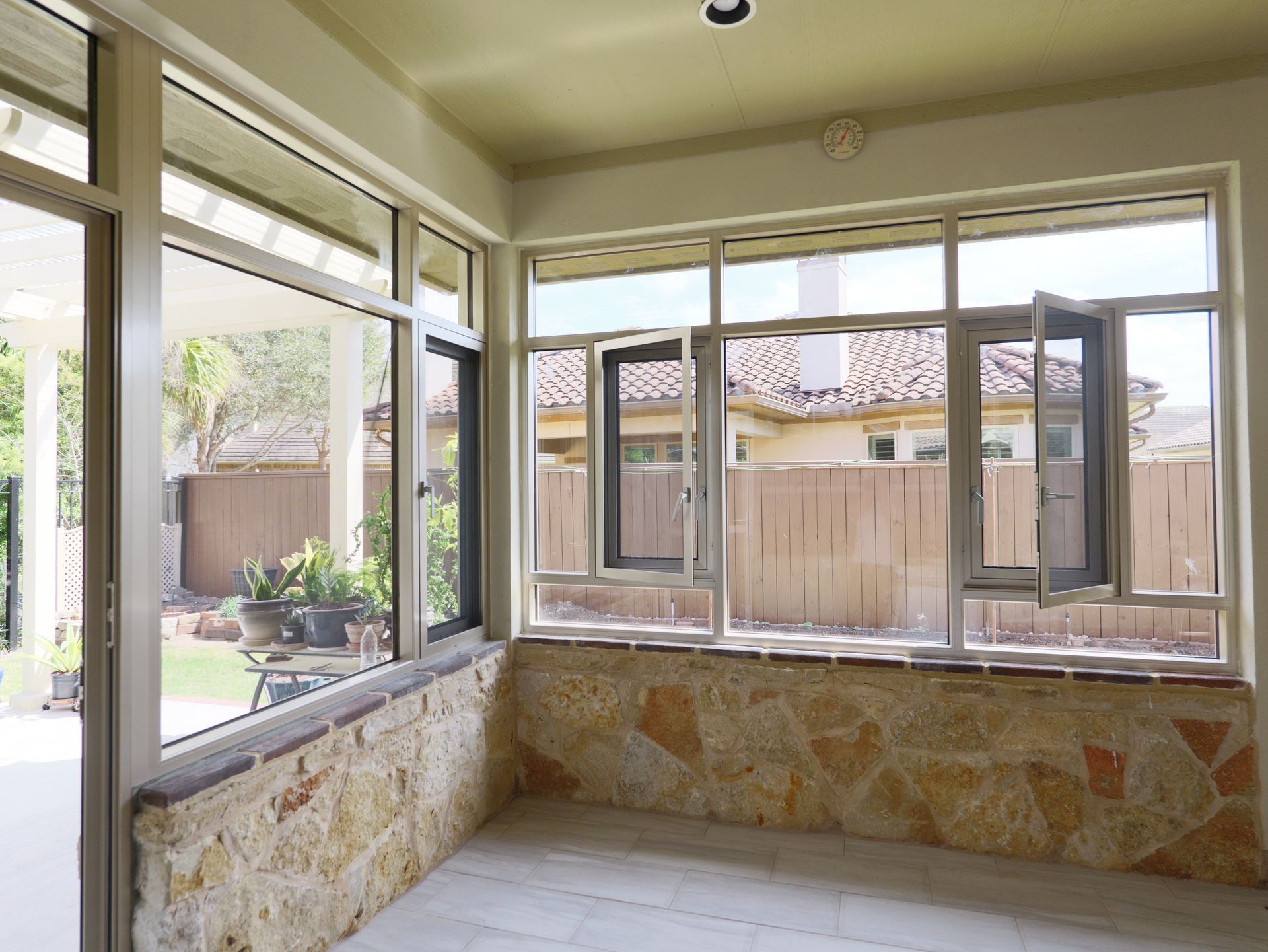 Enclosed patio with stone half-walls and large windows overlooking a backyard and fence.