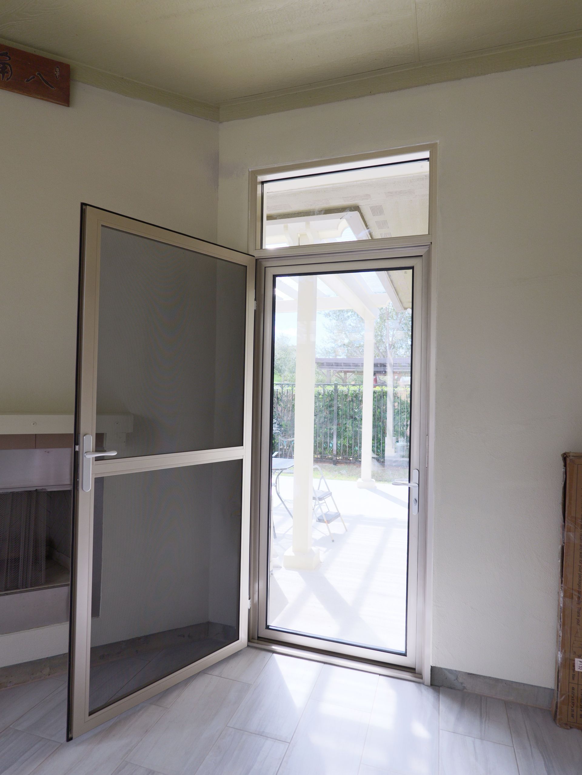 Open screened door leading to a bright outdoor patio from an empty room