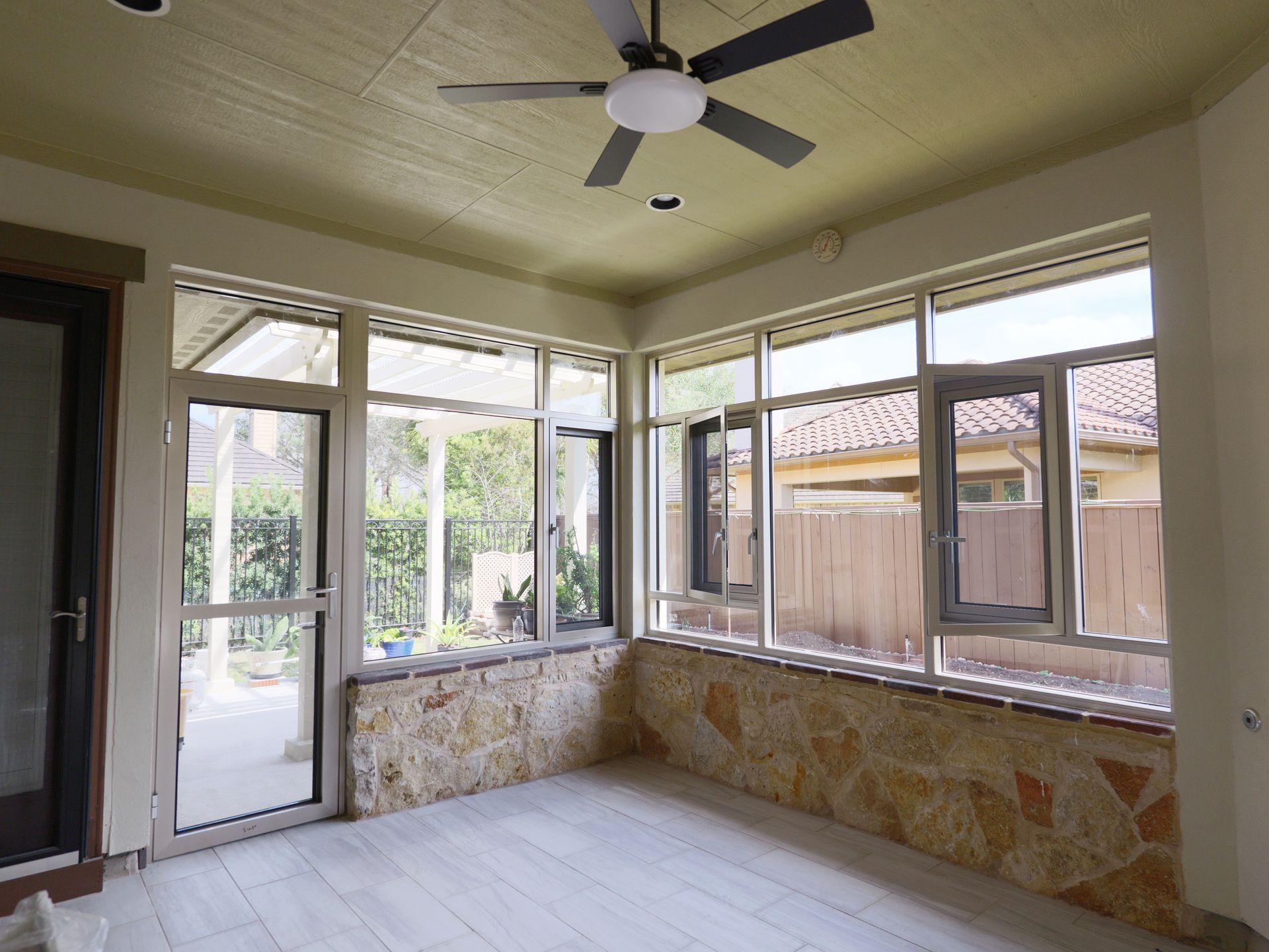 Empty enclosed porch with windows, stone half-walls, and a ceiling fan.