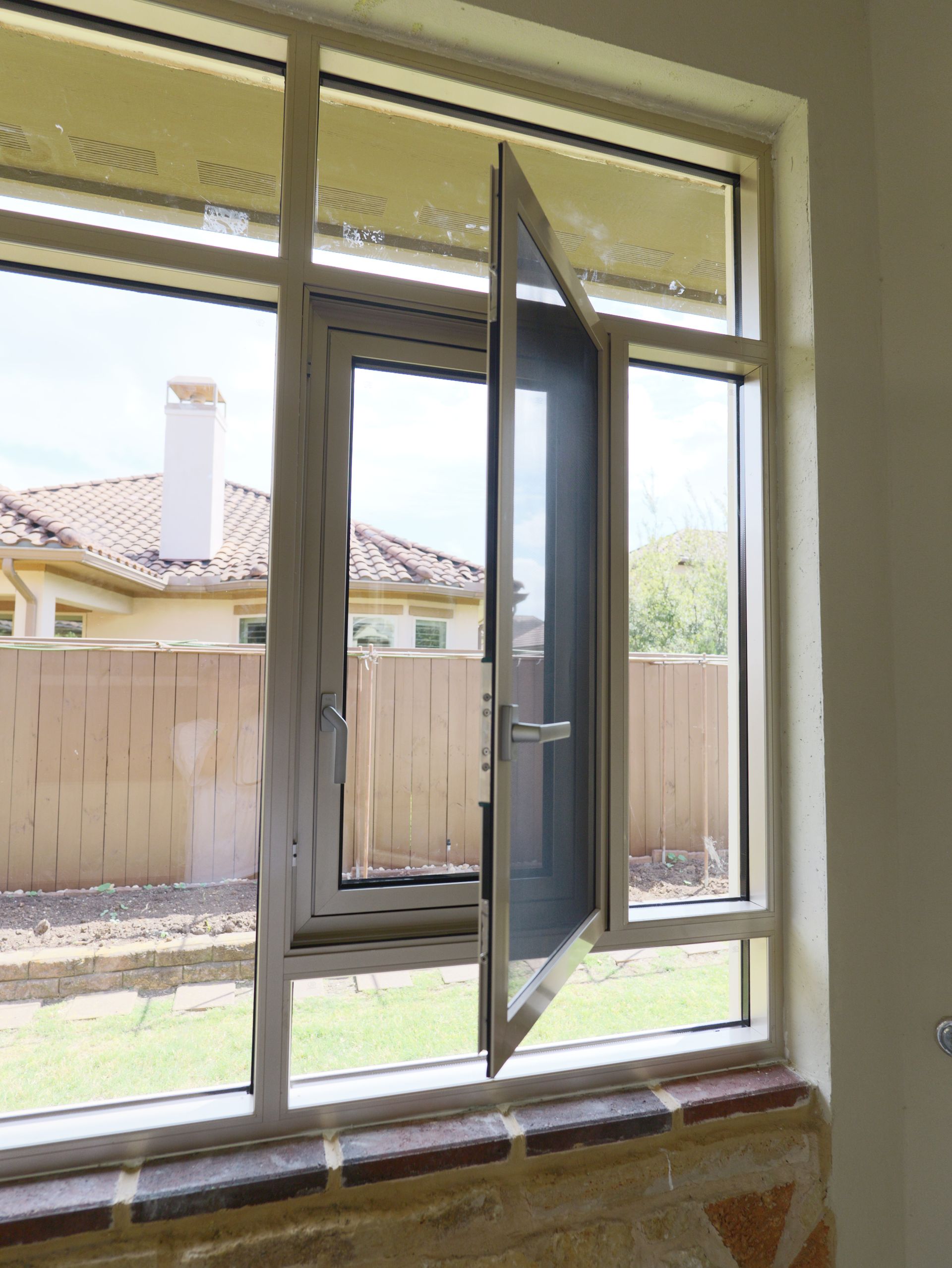 Open window overlooking a backyard and wooden fence, with a house visible outside.