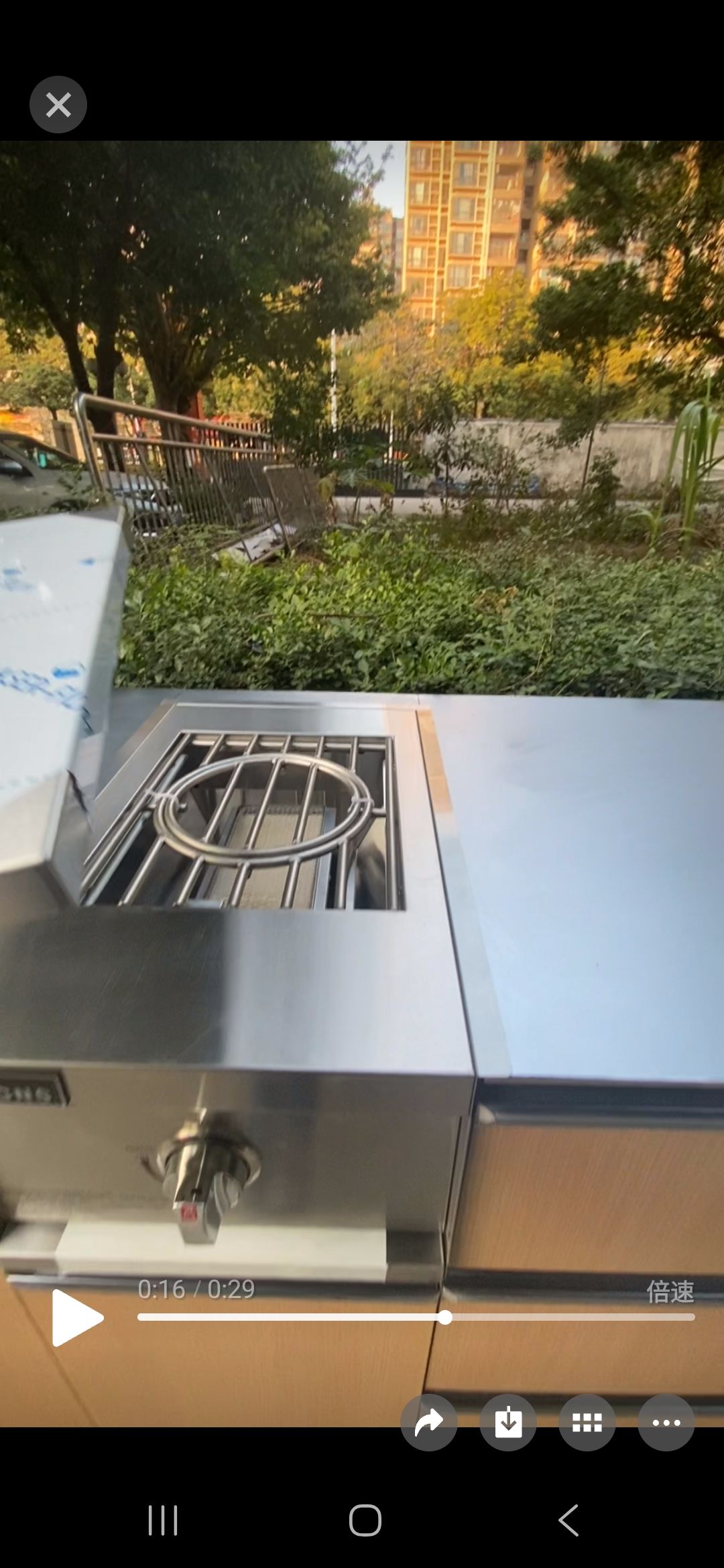Outdoor stainless steel grill on a patio with a leafy garden and building in the background