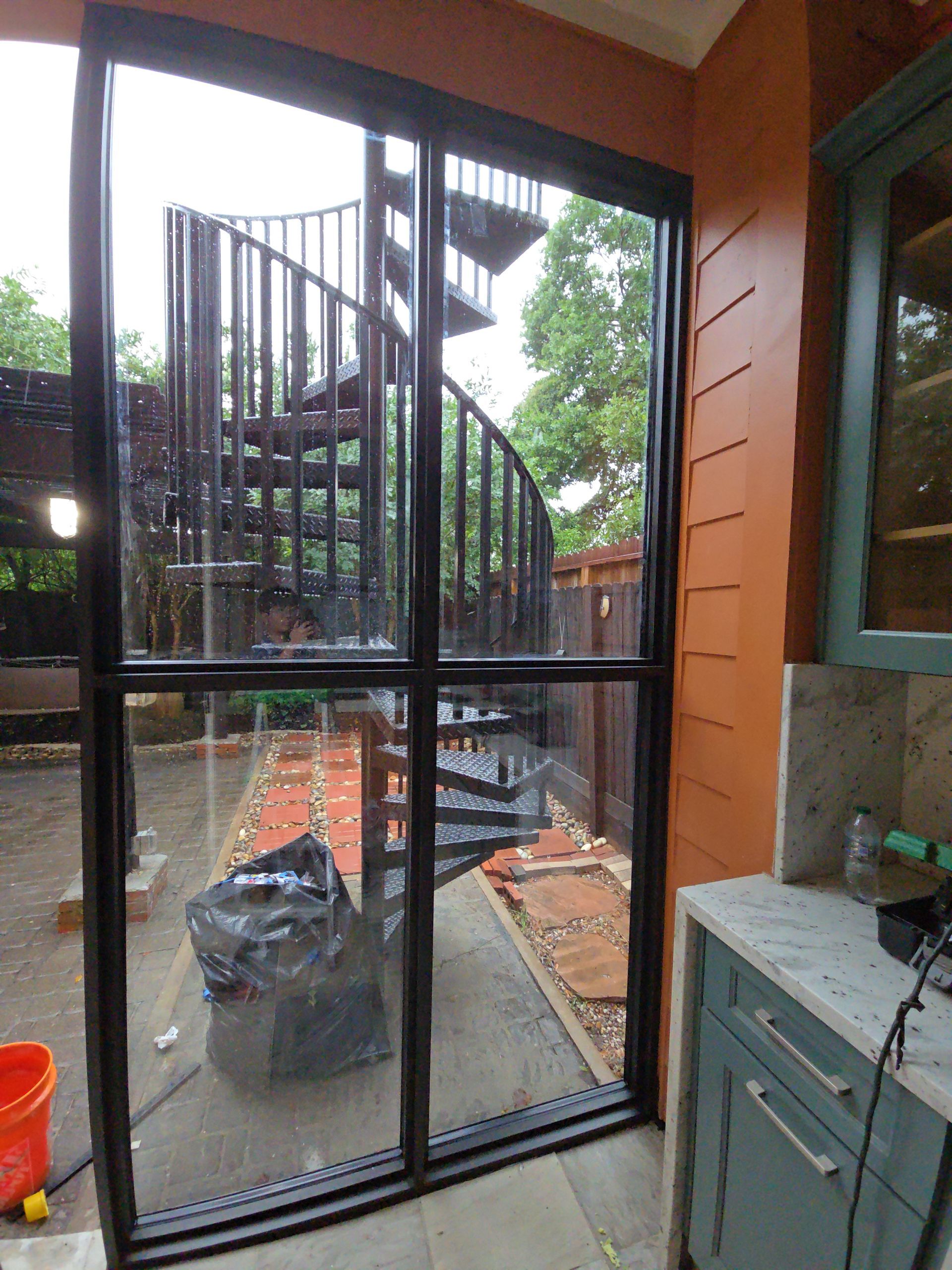 Spiral staircase and outdoor patio seen through a glass door, with construction materials and orange siding nearby