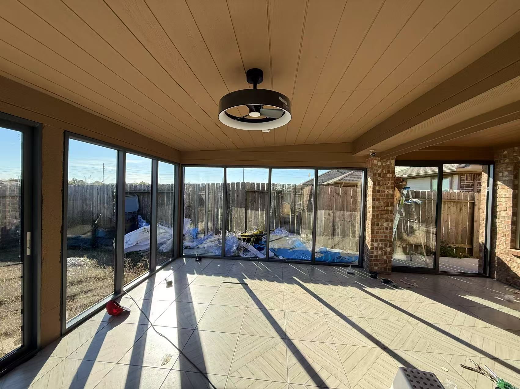 Sunroom with floor-to-ceiling windows, tan ceiling, and sunlight casting long shadows on the floor.
