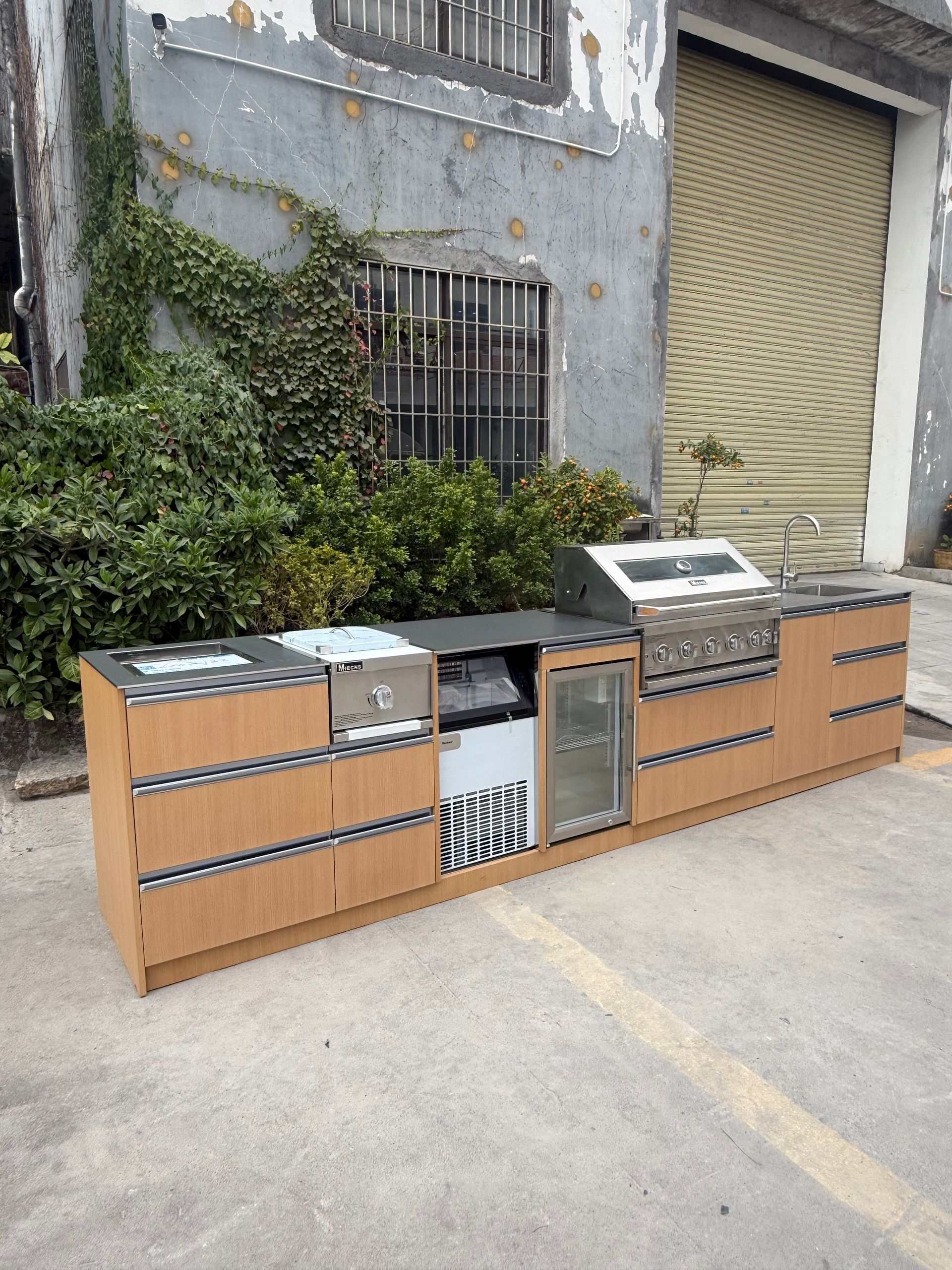 Row of wooden outdoor cabinets and metal units against a gray building wall and closed shutter.