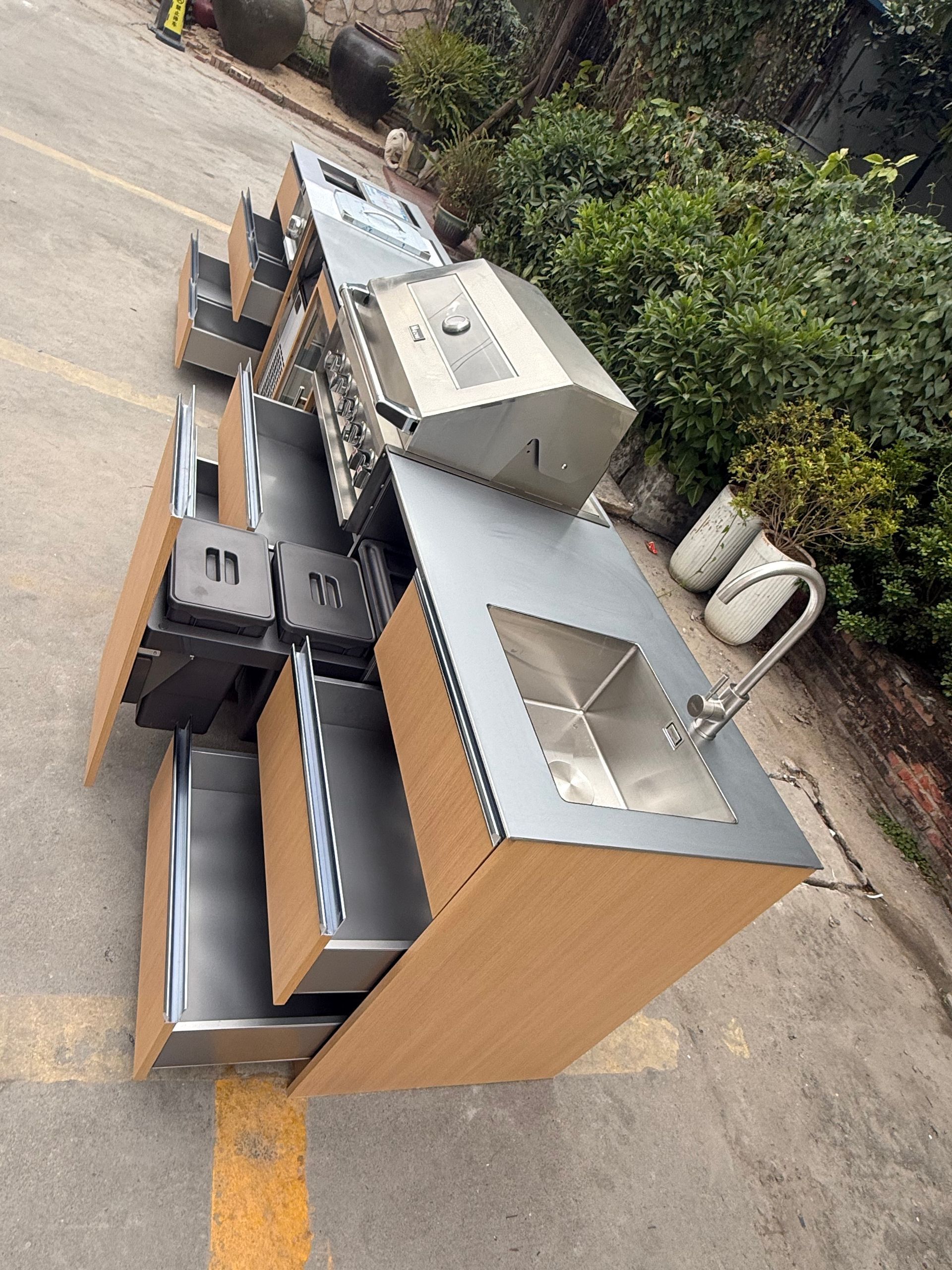 Stacked metal equipment boxes outdoors beside a road, with a silver unit and cardboard packaging.