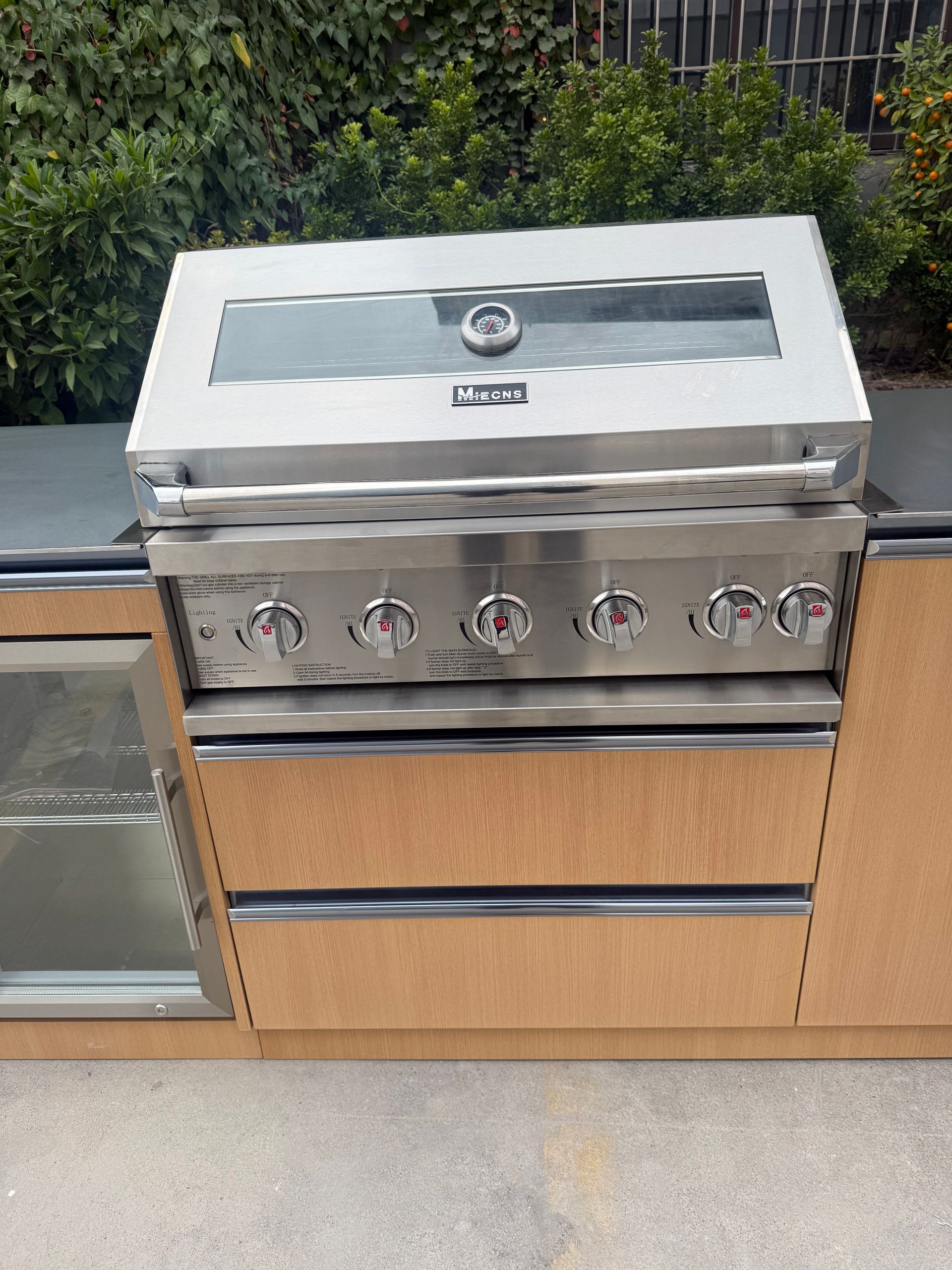 Stainless steel outdoor grill built into a tan cabinet on a patio.