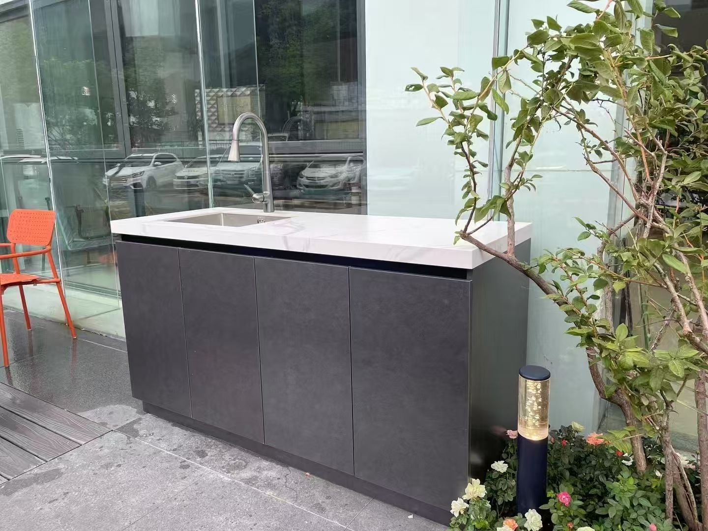 Modern black outdoor cabinet with white countertop beside a glass building entrance and potted plant
