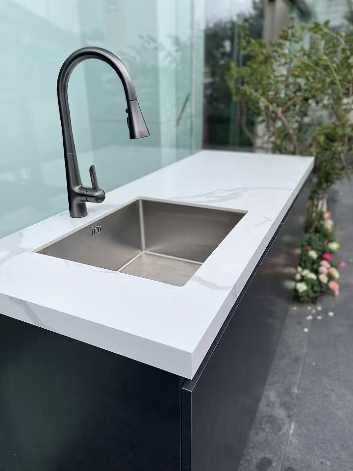 Modern outdoor sink with black faucet and stainless steel basin beside plants and glass wall