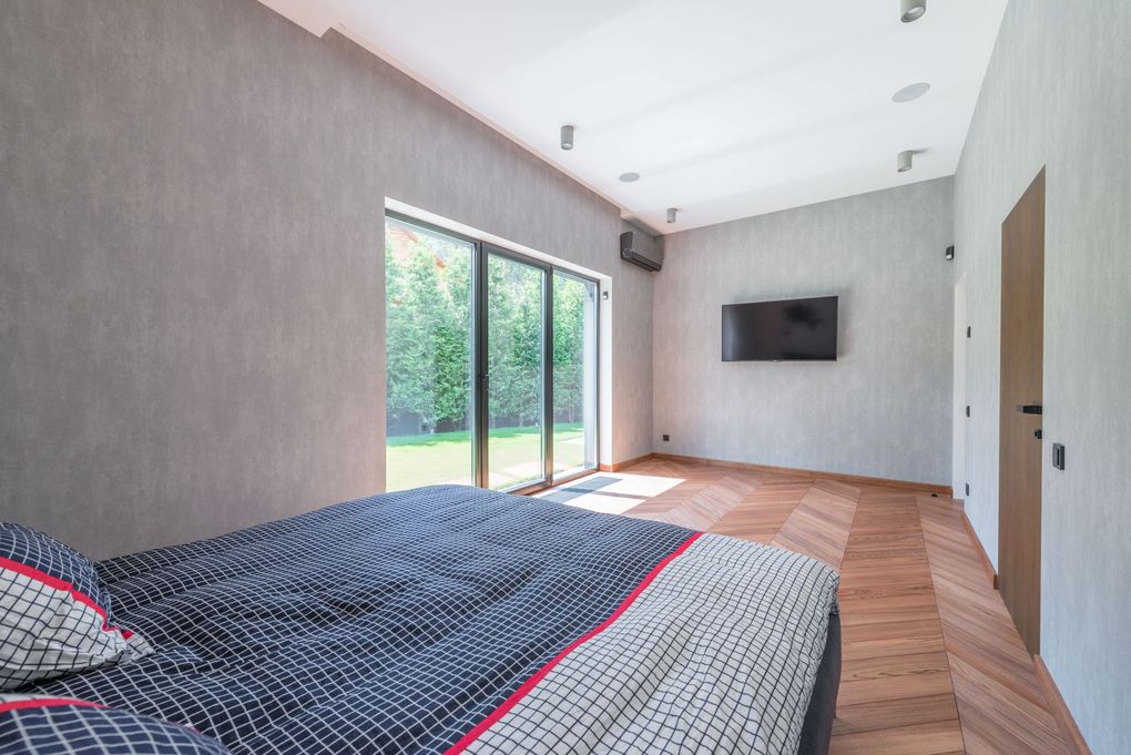 Modern bedroom with a bed, wall-mounted TV, and sliding glass doors to a balcony
