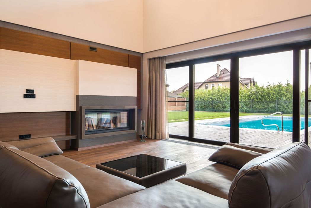 Modern living room with leather sofas, fireplace, and large sliding doors overlooking a pool and garden