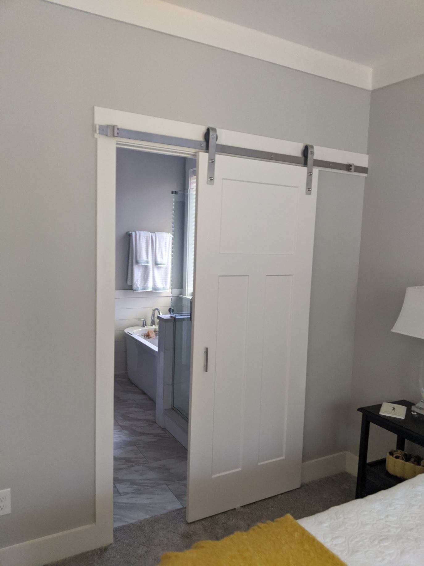 White sliding barn door to a bathroom, gray walls, white trim, and a bed in view.