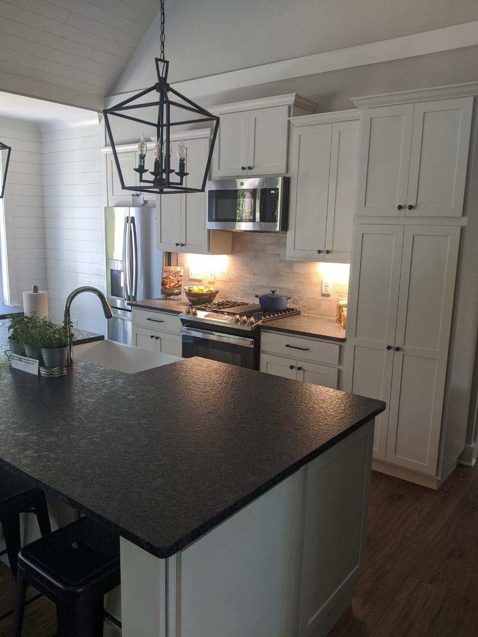 Modern kitchen with white cabinets, black countertop, stainless steel appliances, and an island with bar stools.