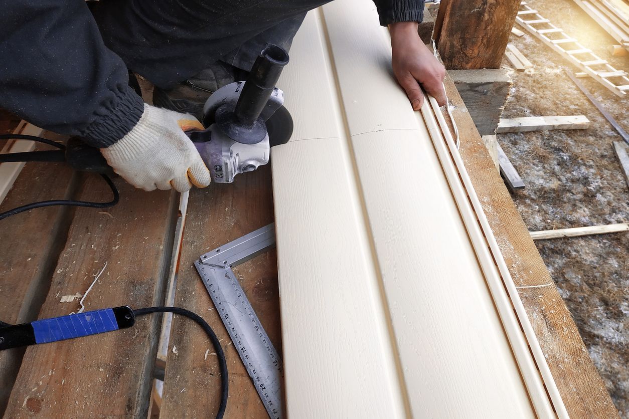Person using an angle grinder to cut siding outdoors on a wooden structure.