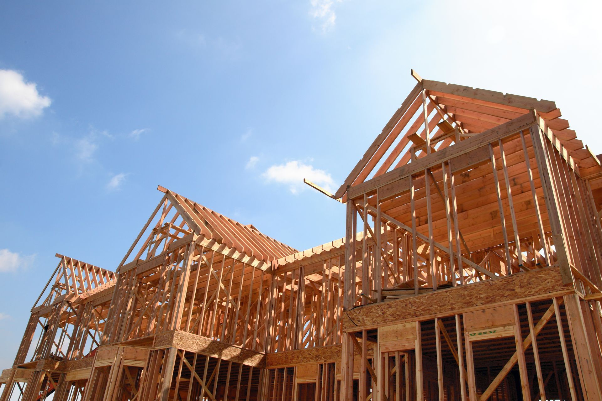 Wooden frame of a house under construction against a blue sky with scattered clouds.
