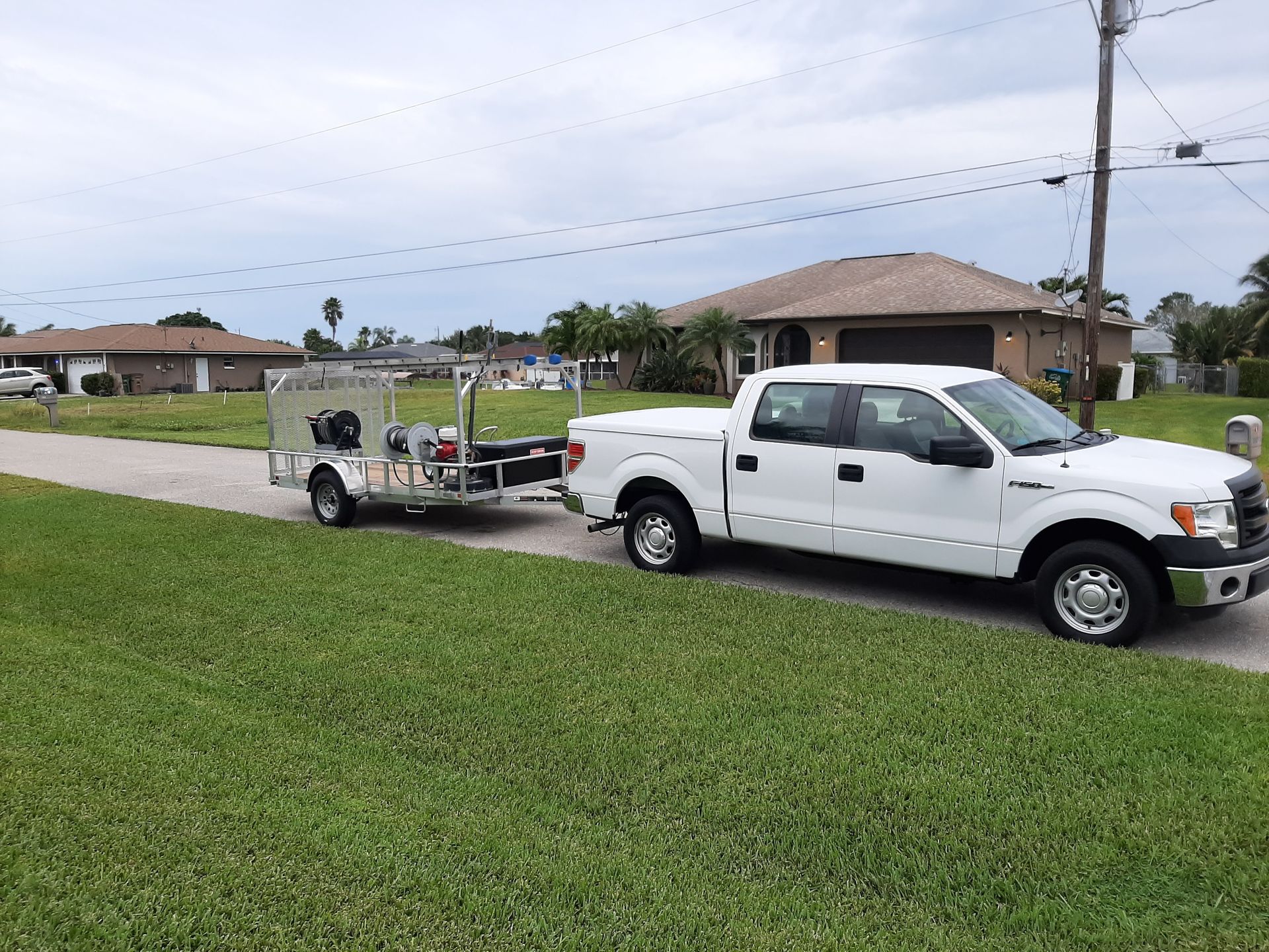 A white truck with a trailer attached to it is parked on the side of the road.