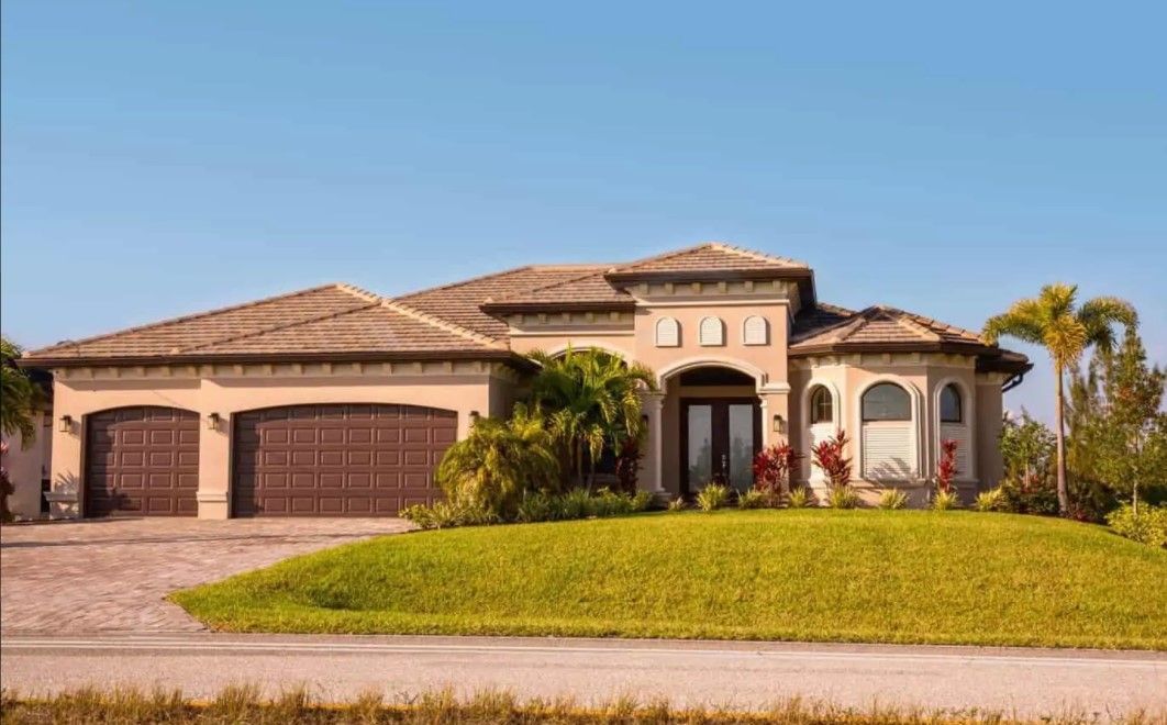 A large house with two garages is sitting on top of a lush green lawn.