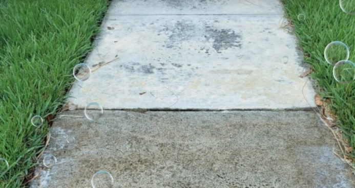 A sidewalk leading to a grassy area with soap bubbles on it.
