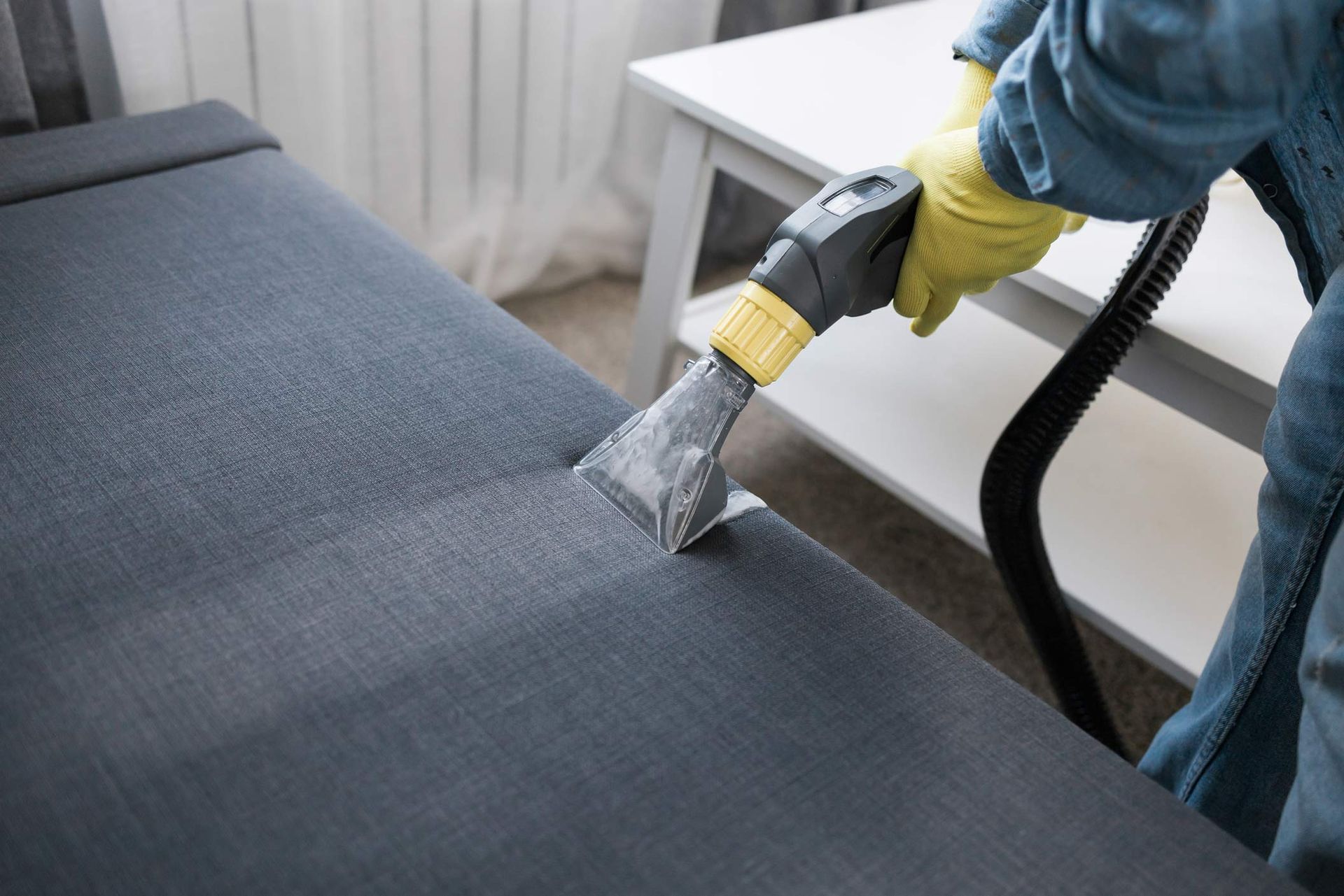 Dry cleaner uses a vacuum machine to clean a stripe of grime off a couch, inside a room.