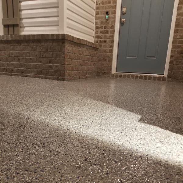 Front porch with speckled concrete floor, brick-and-siding wall, and a closed gray front door at night