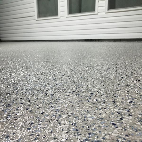 Low-angle view of speckled gray floor beside white vinyl siding and windows.
