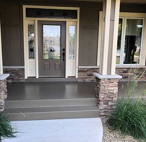 Front porch with steps, stone columns, and a gray front door on a suburban house.