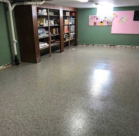 Empty basement room with speckled floor, shelves, and pink bulletin boards on green walls