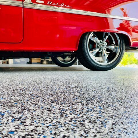 Red classic car with chrome wheel parked on speckled pavement, low-angle view