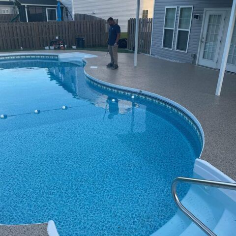 Person standing by a backyard swimming pool beside a house and patio.
