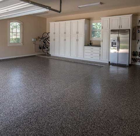 Spacious garage with speckled floor, white cabinets, and stainless steel refrigerator.