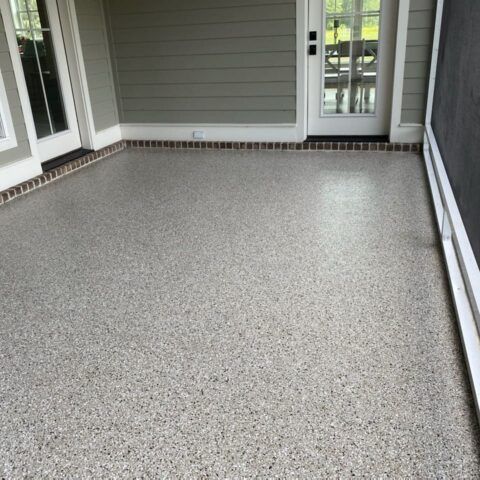 Covered patio with light gray speckled flooring and gray siding, viewed from one corner