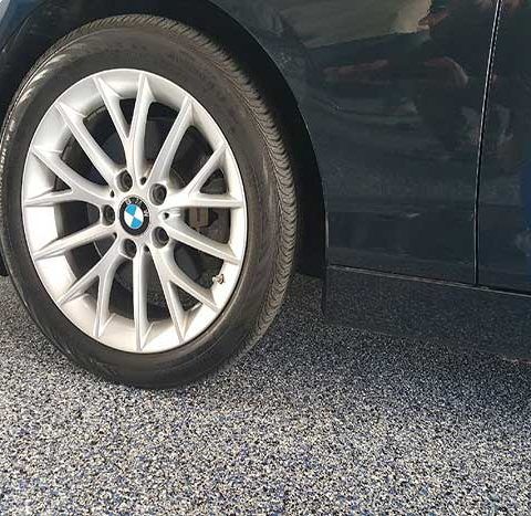 Close-up of a silver alloy car wheel on a dark vehicle parked on concrete floor.