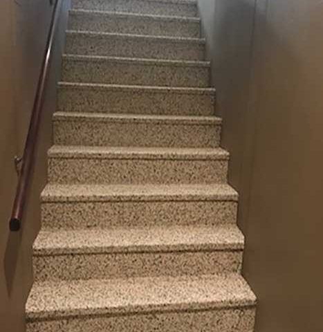 Indoor speckled staircase with brown handrails and beige walls.