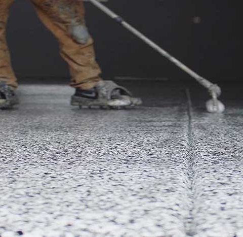 Person using a roller on gray epoxy flooring, smoothing a glossy surface.