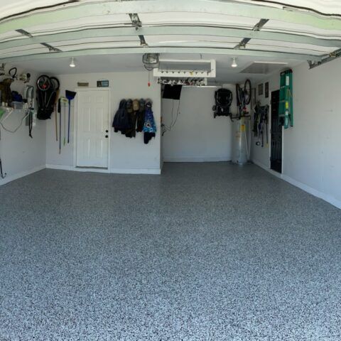 Spacious garage with speckled epoxy floor, white walls, and hanging sports gear and jackets.