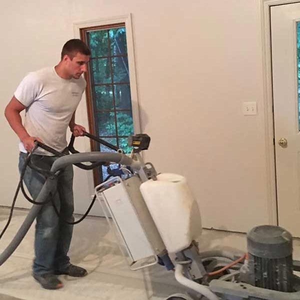 Man operating a floor buffer on a bare indoor floor during renovation