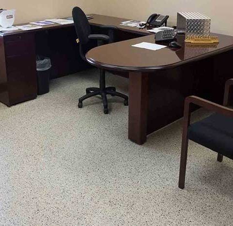 Office cubicle with dark wood desks, black chairs, and a phone on the corner desk.