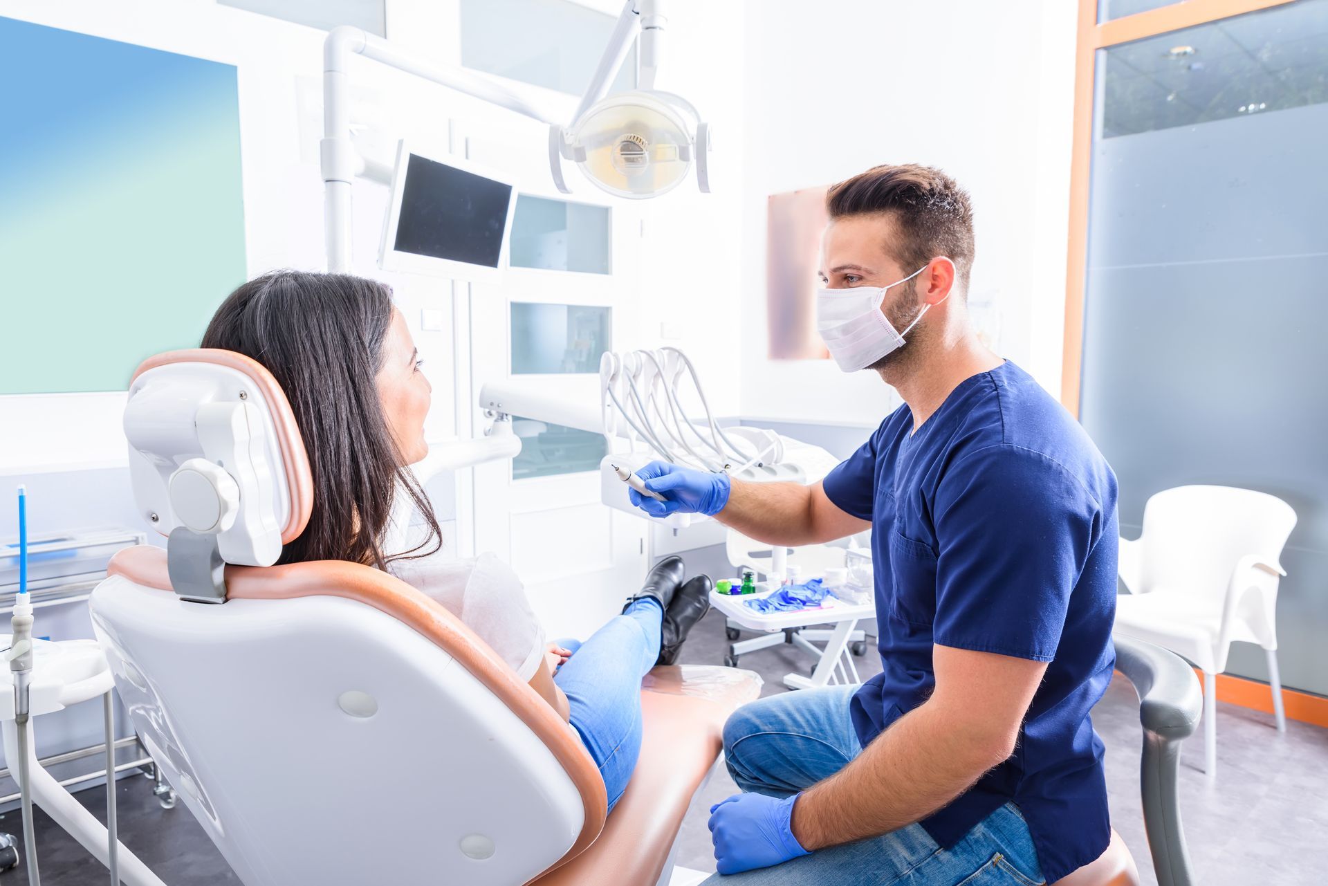 Dentist in mask examining patient reclined in dental chair.