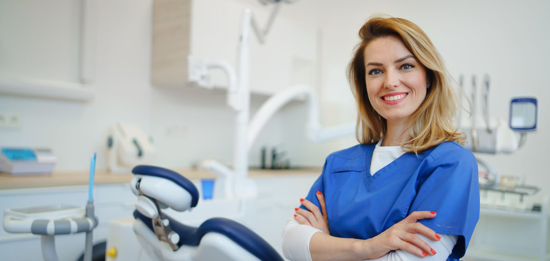 A dentist stands with arms crossed in a dental office setting.